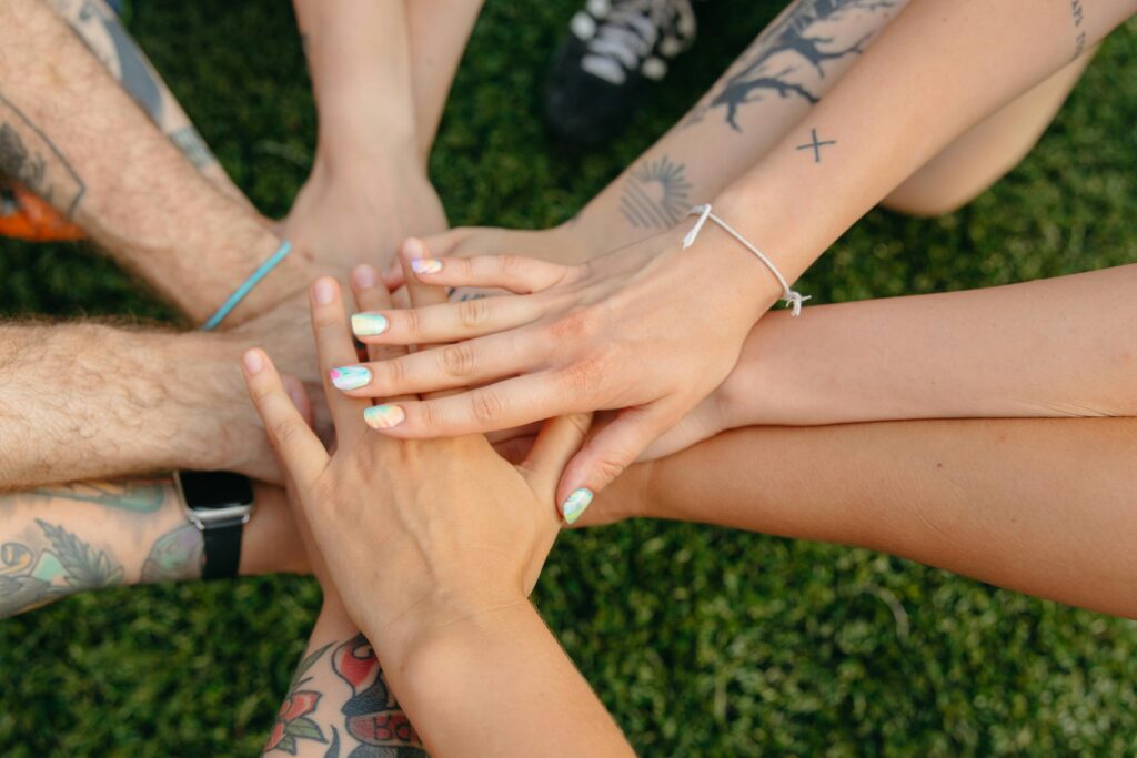 pexels-photo-9501978-9501978 A group of people's hands with tattoos and colorful nails symbolizing unity on grass.